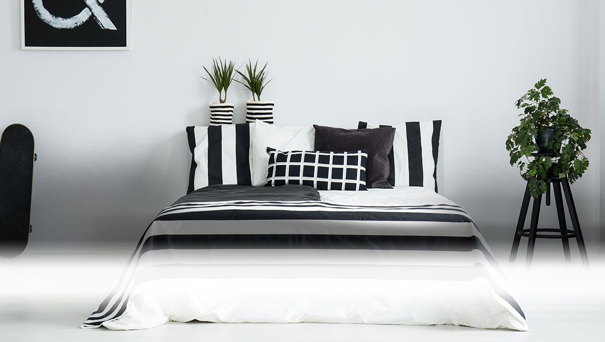 Bedroom set consisting of bed with monochrome bedspread and pillows and plants in black and white planters.